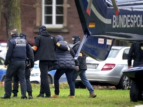 An suspect, second right, is escorted from a police helicopter by police officers after the arrival in Karlsruhe, Germany, Wednesday, Dec. 7, 2022. Thousands of police officers carried out raids across much of Germany on Wednesday against suspected far-right extremists who allegedly sought to overthrow the government in an armed coup. Officials said 25 people were detained.
