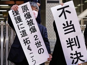 Noboru Sakiyama, left, head of the plaintiffs holds a banner at the Nagasaki District Court in Nagasaki, southern Japan Monday, Dec. 12, 2022. The court on Monday rejected a damages suit filed by a group of children of Nagasaki atomic bombing survivors seeking eligibility for government support for medical cost, saying hereditary radiation impact has not been proven. The banners read " Pave the way to backup Second-Generation Atomic Bomb Survivors," left, and " Unjust Ruling." (Kyodo News via AP)