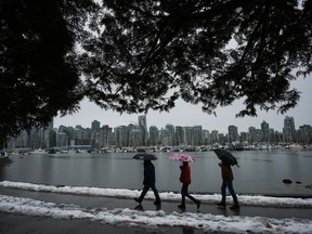 People walk along the Stanley Park seawall as rain falls Sunday, Dec. 25, 2022, while a small amount of snow remains after last week's snowstorm in Vancouver. Flood watches and high streamflow advisories are posted across Vancouver Island and much of British Columbia's inner south coast as heavy rain and high tides raise the risk of flooding after pre-Christmas snowstorms.