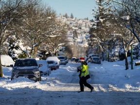 A Canada Post letter carrier crosses a snowy and ice-covered road while delivering mail in Burnaby, B.C., on Wednesday, Dec 21, 2022. A snowstorm dumped more than 30 centimetres of snow in Metro Vancouver this week.