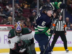 Arizona Coyotes goalie Karel Vejmelka, left, of the Czech Republic, is struck in the mask by the puck as Vancouver Canucks' Brock Boeser stands in front of him during the first period of an NHL hockey game in Vancouver, on Saturday, December 3, 2022.