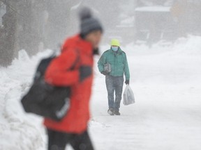 People make their way through the Glebe neighbourhood of Ottawa, Saturday, Dec. 24, 2022. Environment Canada has issued a winter storm warning for the region.