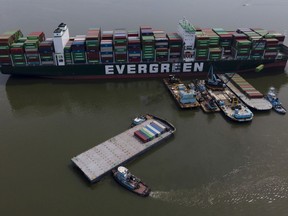 FILE - Tugboats, bottom, align a barge near the container ship Ever Forward, top, which ran aground in March 2022 as workers remove containers from it in efforts to lighten the load and refloat the vessel, April 13, 2022, in Pasadena, Md. The ship has been stuck in the channel since March 13. A Coast Guard investigation into the grounding in March of a cargo ship in the Chesapeake Bay is faulting the pilot tasked with helping the ship navigate the waterway.