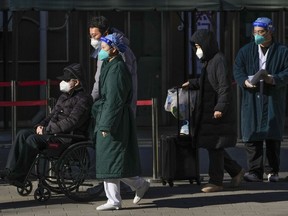Medical workers in protective gear escort an elderly patient on a wheelchair followed by family members as they leave a fever clinic at a hospital in Beijing on Monday, Dec. 19, 2022. A Chinese health official said that the country would only count those who died from pneumonia or respiratory failure in the official COVID death toll, a narrow definition that would certainly limit the numbers of deaths reported, as the country's reopening progresses and cases have soared.