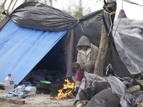 A Venezuelan migrant warms her hands over a campfire outside her makeshift tent refusing to be relocated to a refugee shelter, in Matamoros, Mexico, Friday, Dec. 23, 2022. Migrants are waiting along the U.S.-Mexico border on a pending U.S. Supreme Court decision on asylum restrictions.