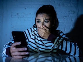 Frightened teenager or young woman using smart mobile cell phone as internet cyberbullying by message stalked abused victim.