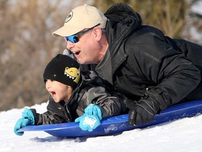 A boy and a man toboggan on a hill beside the Kanata Recreation Centre in Ottawa on Dec. 29, 2022.