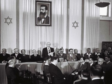David Ben Gurion reads the declaration of independence on May 14, 1948 at the museum in Tel Aviv, below a photo of Theodor Herzl.