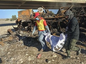 Rescue workers collect remains from the burnt wreckage of a bus accident in Bela, an area of Lasbela district of Balochistan province, Pakistan, Sunday, Jan. 29, 2023. The passenger bus fell into a ravine and caught fire killing dozens people in southern Pakistan on Sunday, a government official said. (AP Photo)
