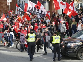 People march past police at a demonstration, part of a convoy-style protest, in Ottawa, on Saturday, April 30, 2022. The Ottawa People's Commission says last winter's weeks-long "Freedom Convoy" protest was a "colossal" violation of residents' rights.