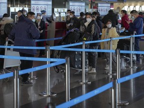 Masked travellers with luggage line up at the international flight check in counter at the Beijing Capital International Airport in Beijing, Thursday, Dec. 29, 2022. An expert says Canada's requirement of a negative COVID-19 test of travellers from China will not help in preventing new variants or the spread of the virus.