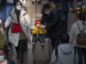 A man pushes a child riding on a suitcase at Beijing West Railway Station in Beijing, Wednesday, Jan. 18, 2023. A population that has crested and is slowly shrinking will pose new challenges for China's leaders, ranging from encouraging young people to start families, to persuading seniors to stay in the workforce longer and parents to allow their children to join the military.