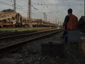 A railway worker sits next to a heavily damaged train after a Russian attack on a train station yesterday during Ukraine's Independence Day in the village Chaplyne, Ukraine, Thursday, Aug. 25, 2022.
