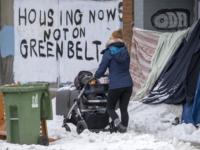 A person pushes a stroller past the shelter of an unhoused person in Toronto on Tuesday Jan. 31, 2023. The federal housing advocate is launching a review of homeless encampments in Canada, calling the situation a human rights crisis fuelled in part by the failure of all levels of government to provide adequate housing.
