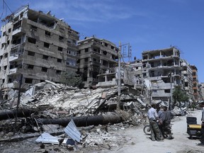 FILE - People stand in front of damaged buildings, in the town of Douma, the site of a suspected chemical weapon attack, near Damascus, Syria, on April 16, 2018. Syria on Thursday Feb. 2, 2023 dismissed the findings of an investigation of which the global chemical weapons watchdog concluded that there were "reasonable grounds to believe" Syria's air force dropped two cylinders containing chlorine gas on the city of Douma in 2018.