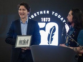 Grand Chief Peter Johnston watches as Prime Minister Justin Trudeau reacts to being given a framed archival photo of his father Pierre and brother Sasha playing on a swing set in Old Crow, Yukon, back in the early 1970s. The picture was presented Sunday Feb. 12, 2023 in Whitehorse at a dinner event during the 50th Anniversary celebration of the Council of Yukon First Nations' document Together Today For Our Children Tomorrow.
