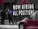 A person standing near a sign indicating that a local business is hiring.