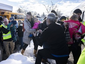 Parents and their children are loaded onto a warming bus as they wait for news after a bus crashed into a daycare centre in Laval, Que., on Wednesday, Feb. 8, 2023.