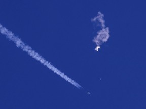 In this photo provided by Chad Fish, the remnants of a large balloon drift above the Atlantic Ocean, just off the coast of South Carolina, with a fighter jet and its contrail seen below it, Saturday, Feb. 4, 2023. The downing of the suspected Chinese spy balloon by a missile from an F-22 fighter jet created a spectacle over one of the state's tourism hubs and drew crowds reacting with a mixture of bewildered gazing, distress and cheering.