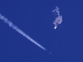 In this photo provided by Chad Fish, the remnants of a large balloon drift above the Atlantic Ocean, just off the coast of South Carolina, with a fighter jet and its contrail seen below it, Saturday, Feb. 4, 2023.