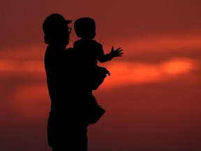 A British Columbia advocacy organization says child poverty decreased in the province in 2020 due to government benefits launched in response to the COVID-19 pandemic, but the progress may be wiped out by rising living costs. A silhouette against the sky of a man holding a child in Kansas City, Mo., Friday, June 26, 2020.