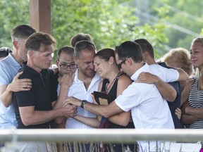 Amélie Lemieux, centre, is comforted by family members as she holds pictures of her two daughters, Romy and Norah Carpentier, at a memorial in Lévis, Que., on Monday, July 13, 2020. The maternal grandmother of two young Quebec girls killed by their father in July 2020 says he was more agitated and nervous in the lead up to killings.