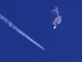 In this photo provided by Chad Fish, the remnants of a large balloon drift above the Atlantic Ocean, just off the coast of South Carolina, with a fighter jet and its contrail seen below it, Feb. 4, 2023. Canadians have been inundated with reports of unidentified objects being shot down by American fighter jets over the U.S. and Canada.