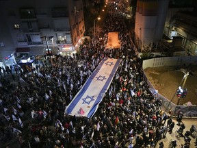 Israelis march with large national flag during a protest against plans by Prime Minister Benjamin Netanyahu's new government to overhaul the judicial system, in Tel Aviv, Israel, Saturday, Feb. 18, 2023.