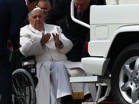Pope Francis speaks with his aides prior to being helped get up the popemobile car from his wheelchair, as he leaves on March 29, 2023 at the end of the weekly general audience at St. Peter's square in The Vatican.