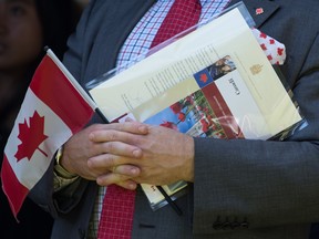 A new Canadian holds a Canadian flag, their citizenship certificate and a letter signed by Prime Minister Justin Trudeau as they sing O Canada after becoming a Canadian citizen during a special Canada Day citizenship ceremony in West Vancouver on Monday, July 1, 2019.