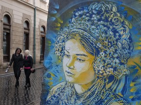 Women walk past a mural in the blue and yellow of the Ukrainian flag depicting a woman in traditional folk dress in Lviv, Ukraine. While Lviv, located in western Ukraine, lies far from the current fighting raging between Ukrainian and Russian armed forces in the east and even offers a sense of normalcy in every day life, it nevertheless remains deeply affected by the war.