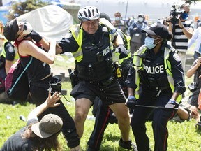 Police remove encampment supporters as they clear Lamport Stadium Park encampment in Toronto on Wednesday July 21, 2021.&ampnbsp;Toronto's ombudsman says the city caused undue harm and showed a lack of dignity and respect for people living in parks when it cleared three homeless encampments in summer 2021.