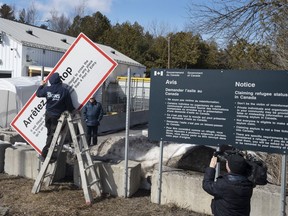 Workers remove warning signs at the irregular border at Roxham Road from New York into Canada on Friday, March 24, 2023, in Champlain, N.Y.