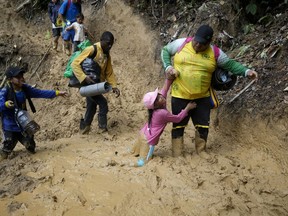 FILE - A woman lifts a child from a muddied path as Ecuadorian migrants walk across the Darien Gap from Colombia into Panama hoping to reach the U.S., on Oct. 15, 2022. A report released Wednesday, March 22, 2023, by Panama´s ombudsman and two United Nations organisms pointed to a rise in the number of migrant minors crossing the Darien area.