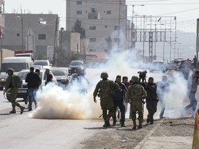 Palestinian journalists run away from tear gas fired by Israeli soldiers towards Palestinians after they attack Israeli cars in the West Bank town of Hawara, Friday, March 3, 2023.