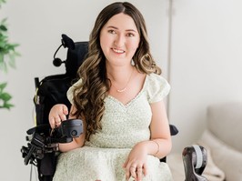 Tori Hunter, an advocate for those living with spinal muscular atrophy, sits smiling for the camera. She has long, wavy brown hair and is wearing a light green and white dress.
