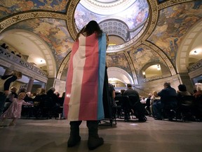 FILE - Glenda Starke wears a transgender flag as a counterprotest during a rally in favor of a ban on gender-affirming health care legislation, March 20, 2023, at the Missouri Statehouse in Jefferson City, Mo. Minors in Missouri soon will be required to undergo 18 months of therapy before receiving gender-affirming health care under an emergency rule released Thursday, April 13, 2023, by the state's Republican attorney general.