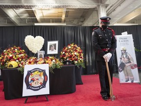A fireman stands as honour guard beside the urn of Pierre Lacroix during a visitation Thursday, October 28, 2021 in Montreal.&ampnbsp;A Quebec coroner says Montreal firefighters need better training and equipment for water rescues in her report on the 2021 drowning of firefighter Lacroix.THE CANADIAN PRESS/Ryan Remiorz
