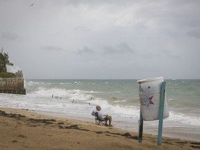 FILE - A man sits in front of a beach watching as the waves break before the arrival of Tropical Storm Fiona in San Juan, Puerto Rico, Sept. 17, 2022. Puerto Rico's governor declared a state of emergency on April 11, 2023 given worsening coastal erosion across the U.S. territory that officials blame on climate change.