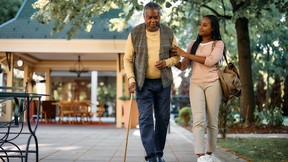 senior man with walking cane and his daughter taking a walk through the park of a nursing home to keep dementia and alzheimers at bay