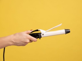 Closeup side view of woman hand holding showing iron curler, professional curling tongs, beauty care concept and hairstyling