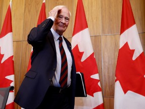 David Johnston walks indoors in front of a row of Canadian flags