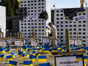 A man walks by Ukrainian flags, crosses with names of victims and a mock-up of bombed buildings which are part of an art installation depicting the consequences of Russian war crimes in Ukraine, at a Soviet military cemetery in Warsaw, Poland on May 9, 2023.