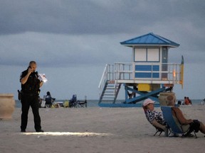 A police officer shines his flashlight downward as he pauses on Hollywood Beach while investigating a shooting Monday, May 29.