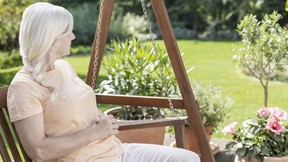 Relaxed senior woman with multiple sclerosis on hanging chair in the garden during summer