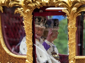 King Charles lll waves from the carriage beside Queen Camilla during the Royal Procession following the King's Coronation, in London on Saturday, May 6, 2023.