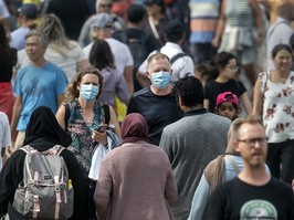 Two people wearing masks while walking in a crowd.