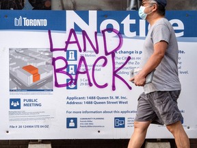 Man walks in front of municipal notice board with Land Back graffiti