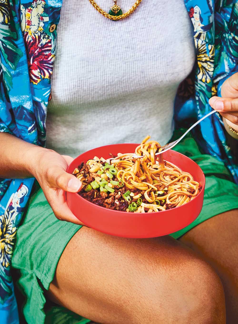 A person eating a bowl of dan dan noodles outdoors