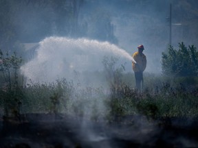 A firefighter directs water on a grass fire on an acreage behind a residential property in Kamloops, B.C., Monday, June 5, 2023. More firefighters from abroad are expected to arrive Wednesday in Canada as the country grapples with its worst wildfire season of the 21st century.